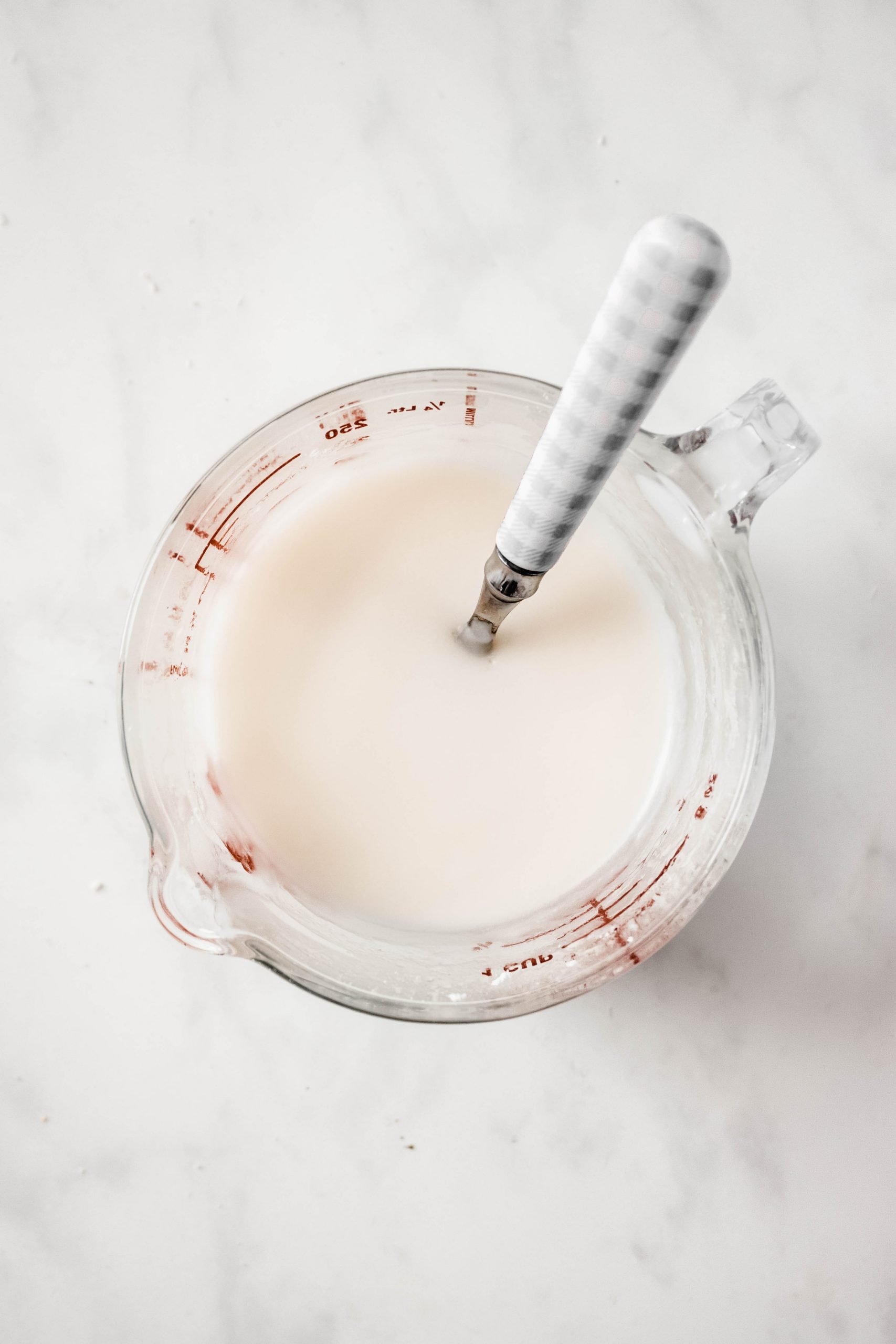 Small glass measuring cup with icing mixed and a spoon resting in it. 