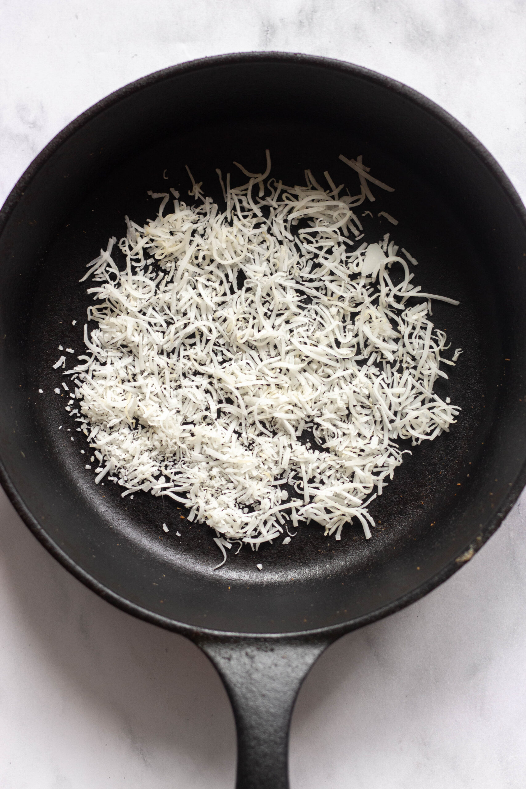 coconut flakes being toasted in a cast iron skillet