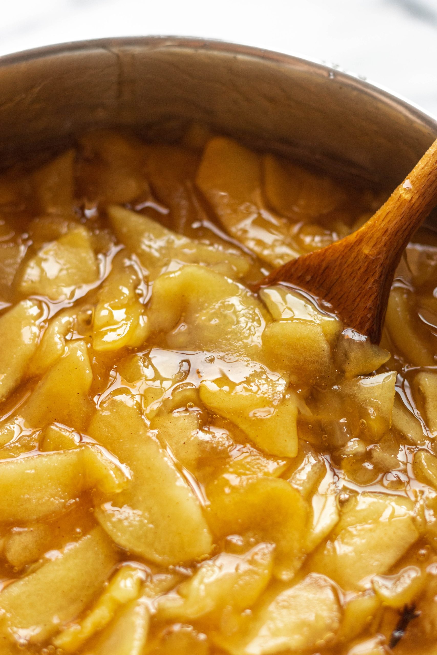 Apples in a pan being stirred with a wooden spoon.