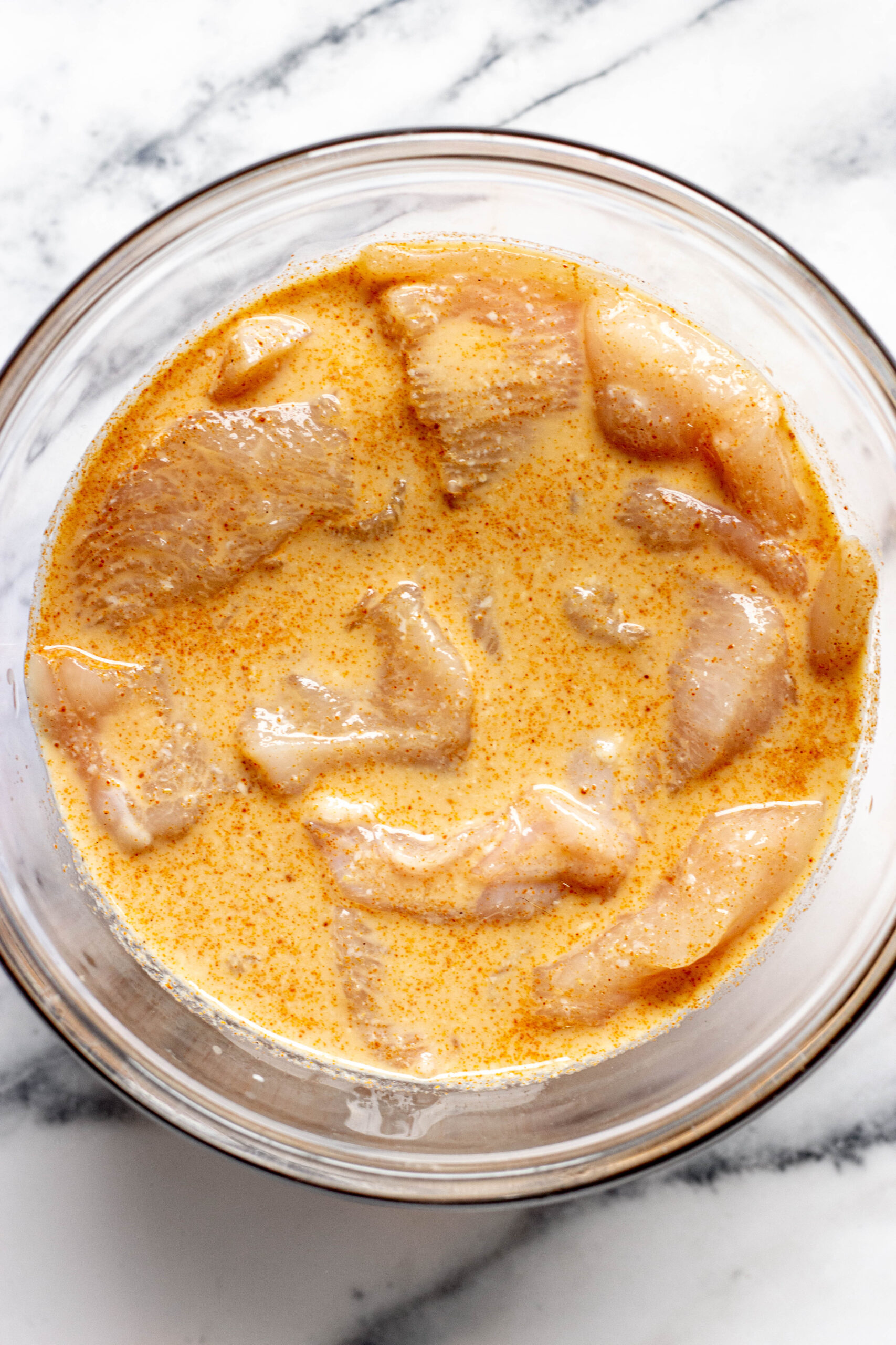 Glass bowl of buttermilk marinade with chicken tenders in it.