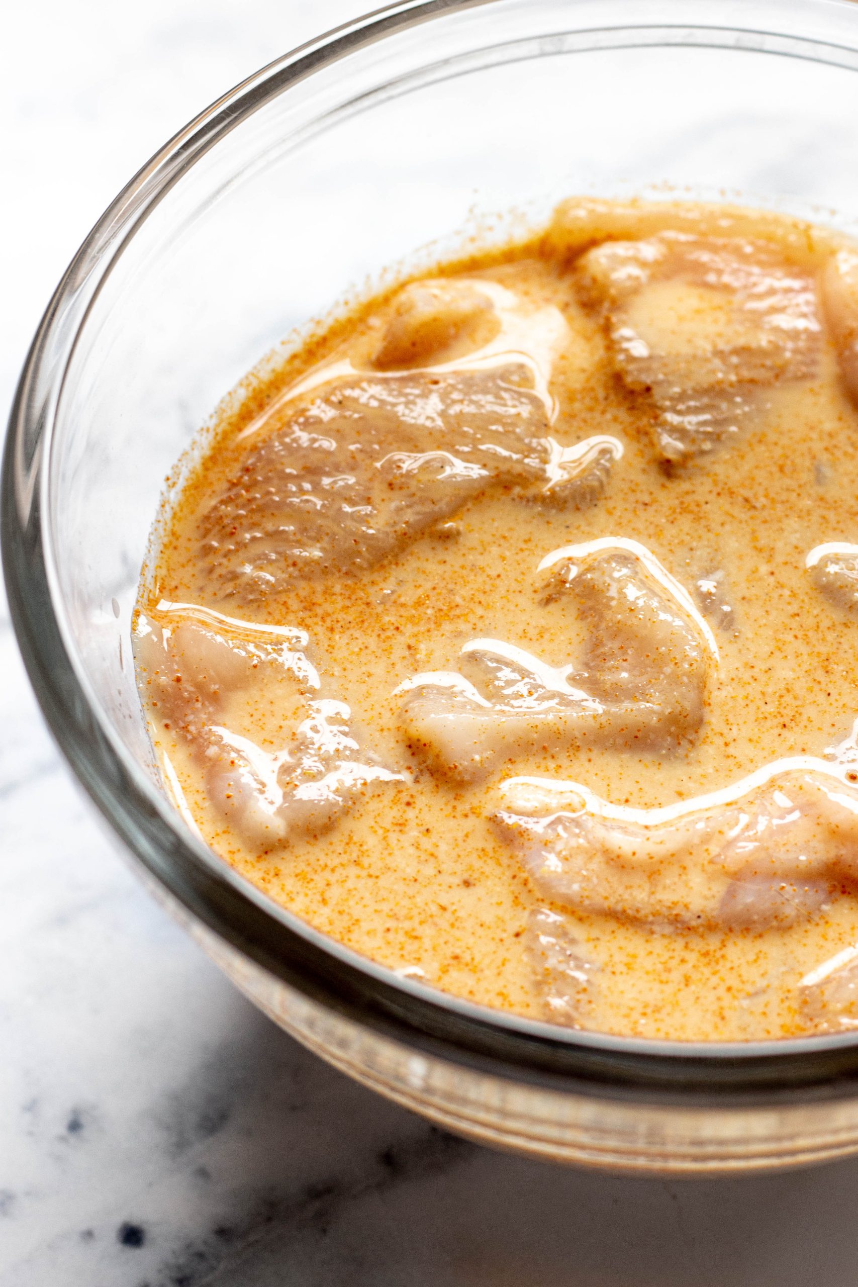 Glass bowl full of chicken tenders marinating in buttermilk marinade.