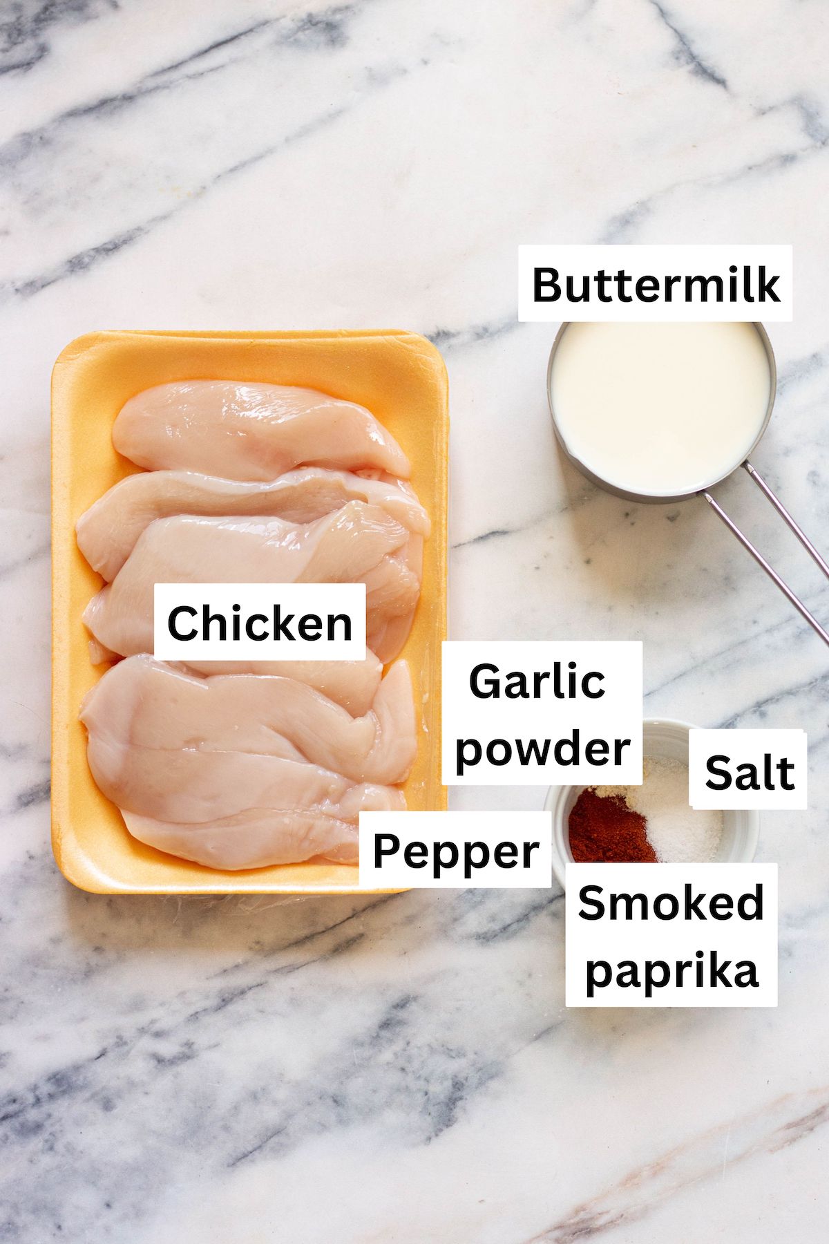 ingredients for buttermilk chicken marinade including raw chicken tenders, a cup of buttermilk, garlic powder, salt, pepper, and smoked paprika