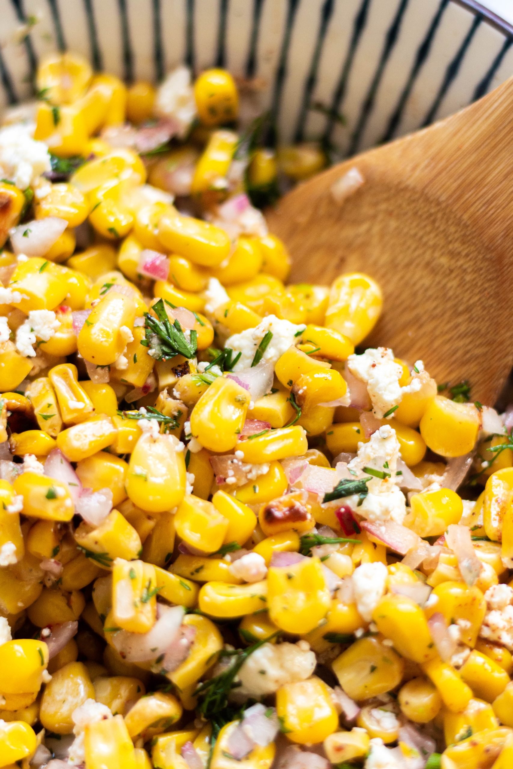freshly mixed grilled corn salad being stirred with a wooden spoon.