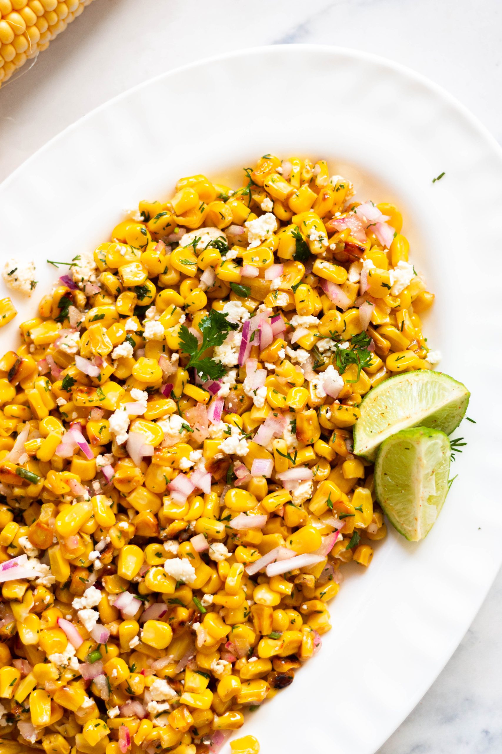 fresh grilled corn salad on a white plate with sliced limes.