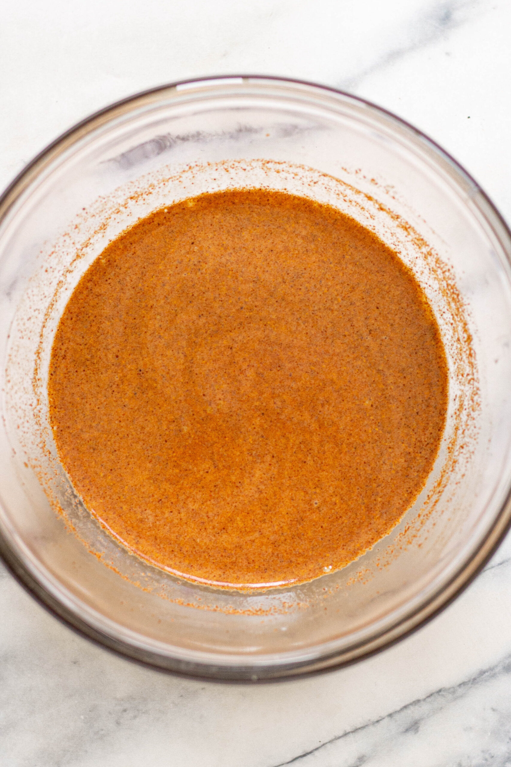 Glass bowl of freshly mixed buttermilk marinade for chicken with paprika, garlic powder, salt and pepper mixed in.