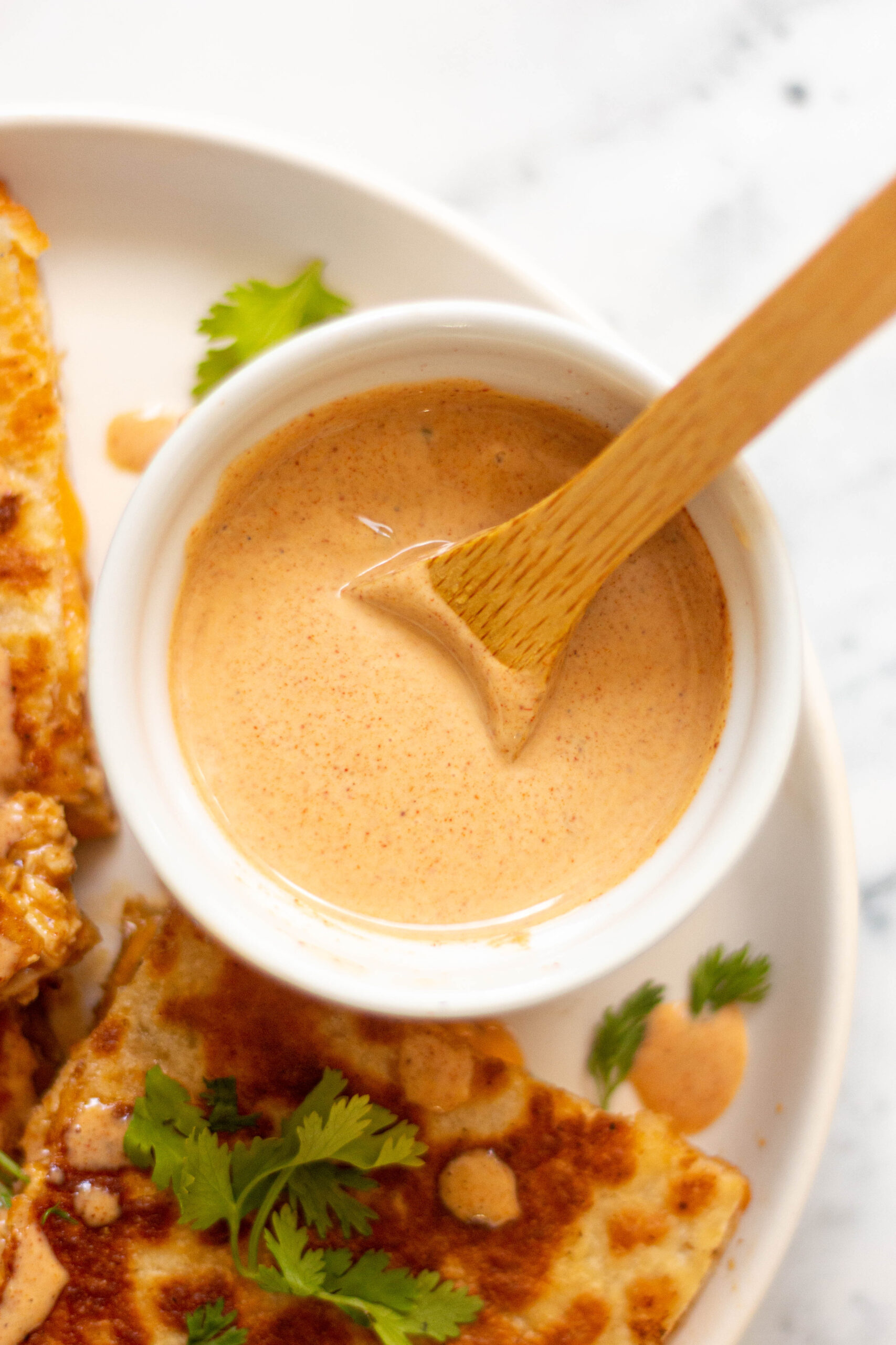 Ramekin with Taco Bell's chicken quesadilla sauce placed on a plate with chicken quesadilla wedges.