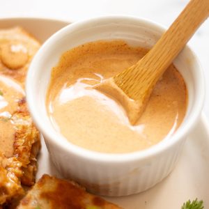 Small ramekin filled with lots of creamy taco bell chicken quesadilla sauce being stirred with a small wooden spoon