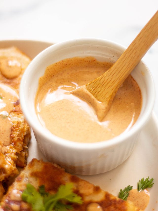 Small ramekin filled with lots of creamy taco bell chicken quesadilla sauce being stirred with a small wooden spoon